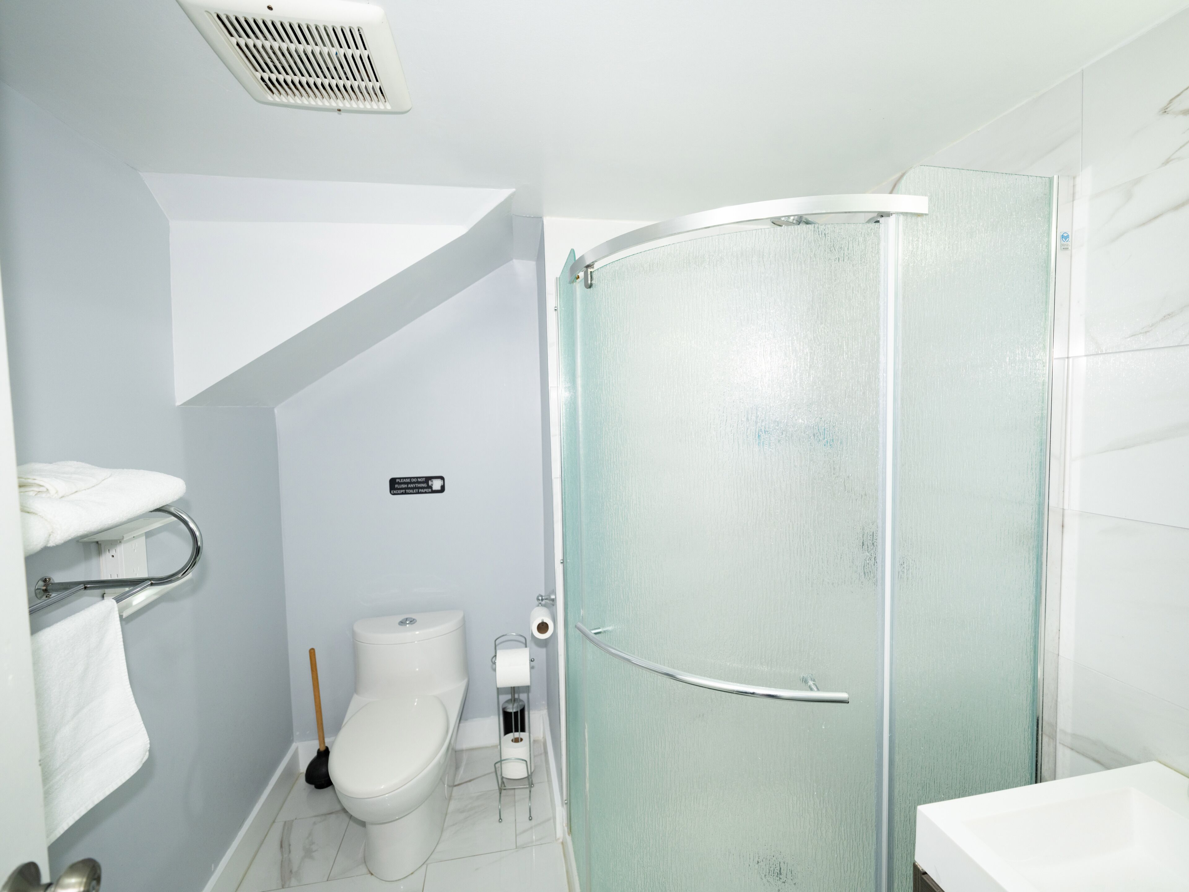 A bathroom with a toilet, a shower, a towel rack, and a toilet paper holder.