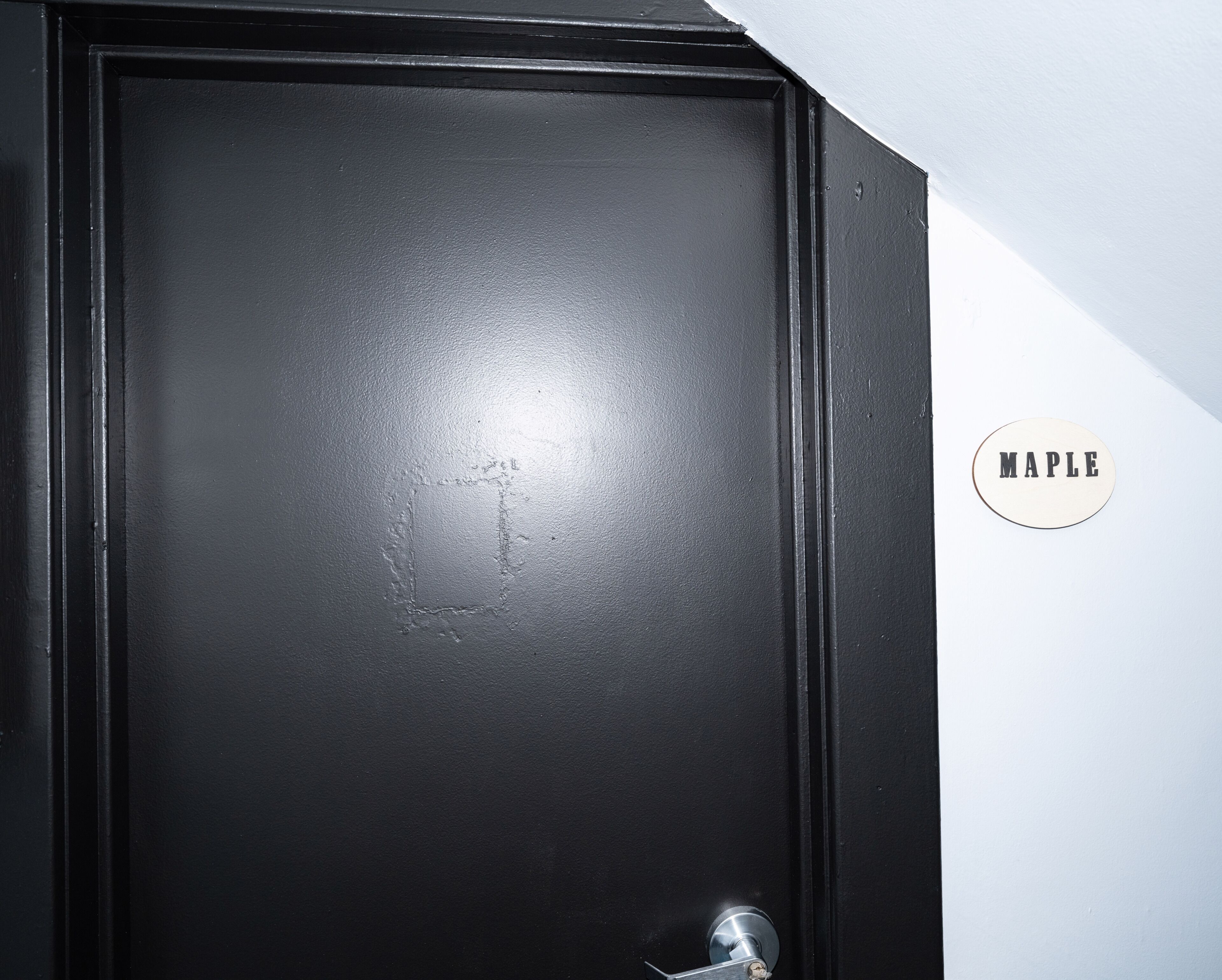 A black door with a metal handle and a circular sign with the word 'MAPLE' on it.