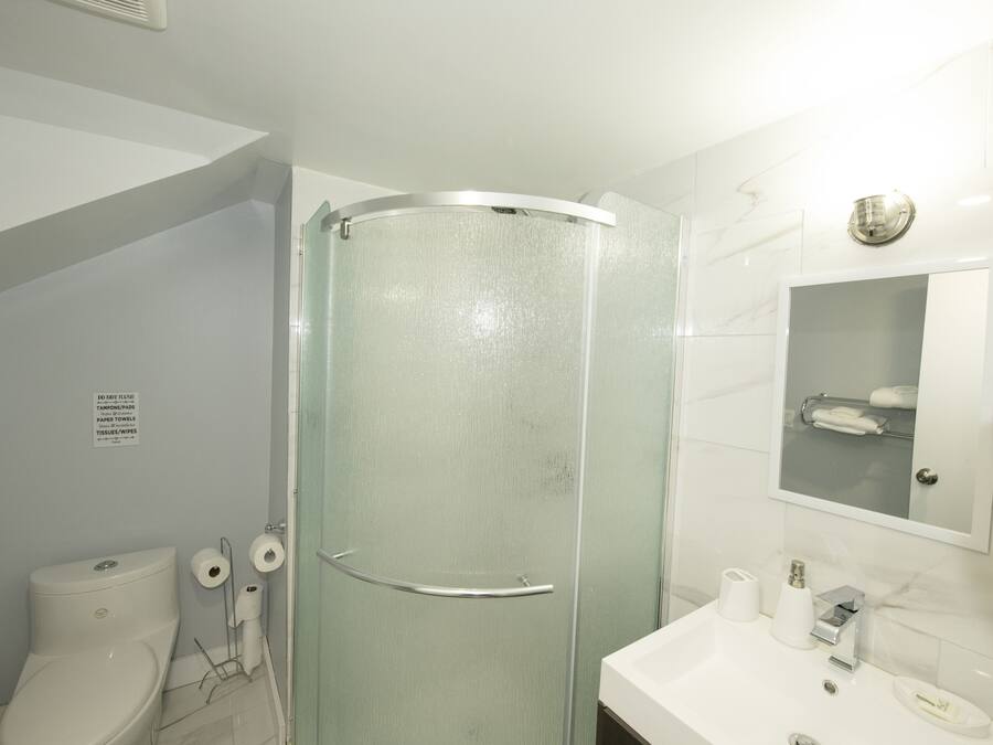 Un baño con ducha de vidrio, inodoro y lavamanos con espejo superior.
