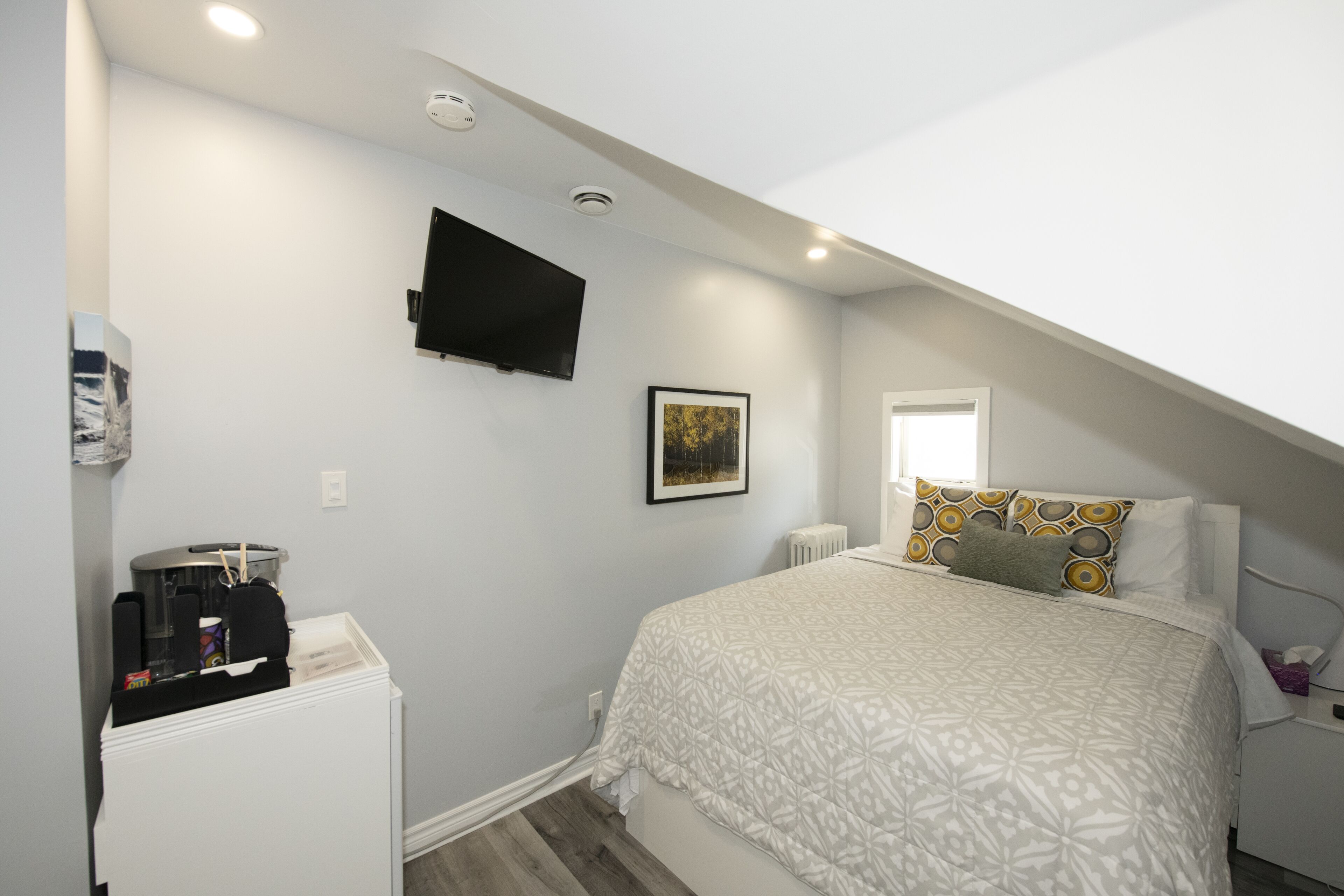 Une chambre à coucher avec un lit, un téléviseur à écran plat fixé au mur, un tableau encadré et une fenêtre.