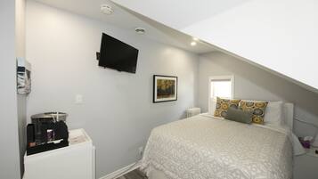 Une chambre à coucher avec un lit, un téléviseur à écran plat fixé au mur, un tableau encadré et une fenêtre.