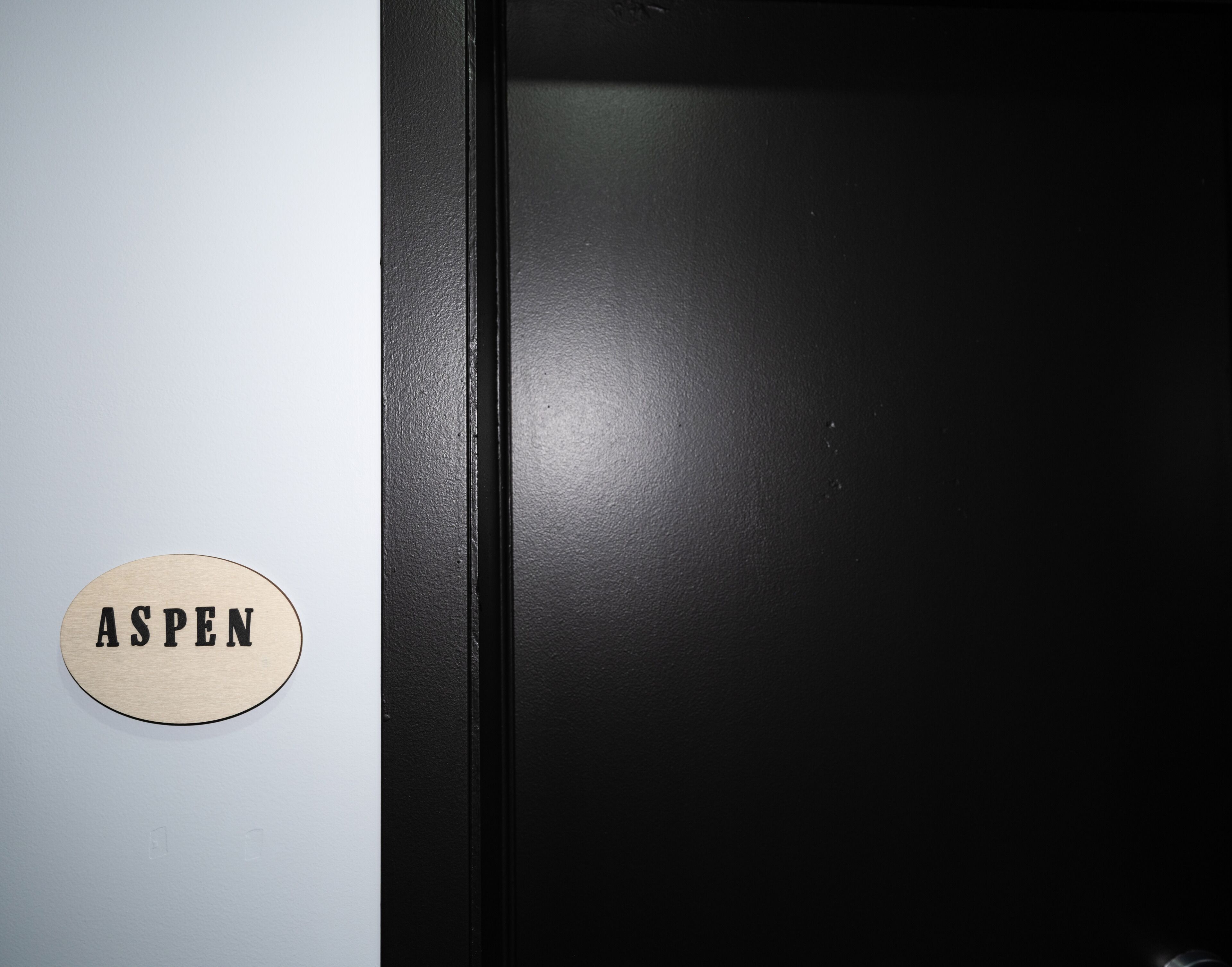 A door with a wooden plaque reading 'ASPEN' on a light-colored wall.