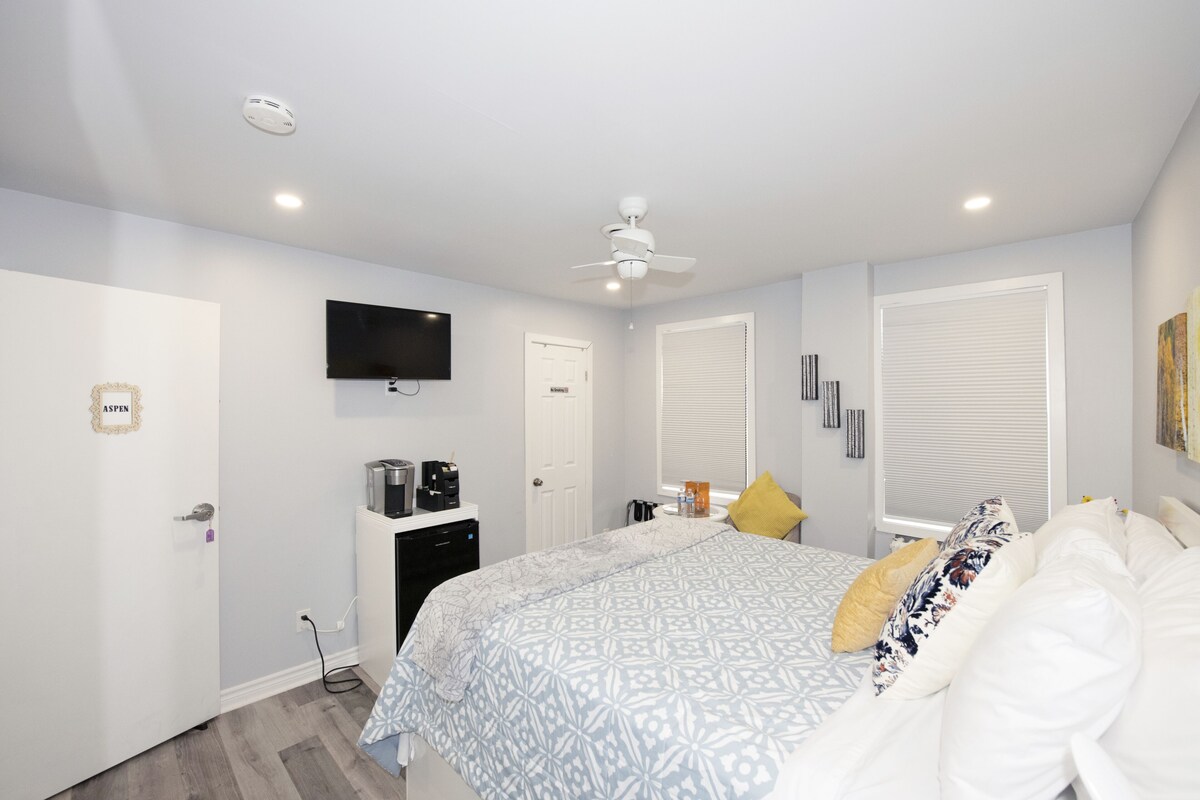 A bedroom with a bed, a ceiling fan, a TV mounted on the wall, and a door labeled "ASPEN".
