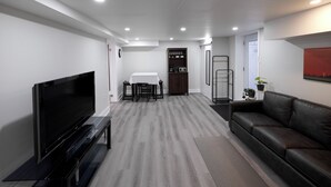 A modern living room with a flat-screen TV, a sofa, a dining table with chairs, and a cabinet with glassware. - Serene Niagara Inn (Niagara Falls)