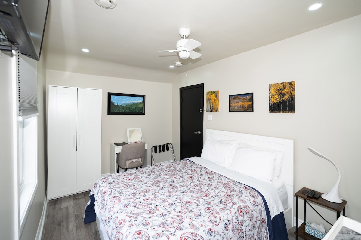 A bedroom with a bed, a desk, a chair, a wardrobe, and a ceiling fan.