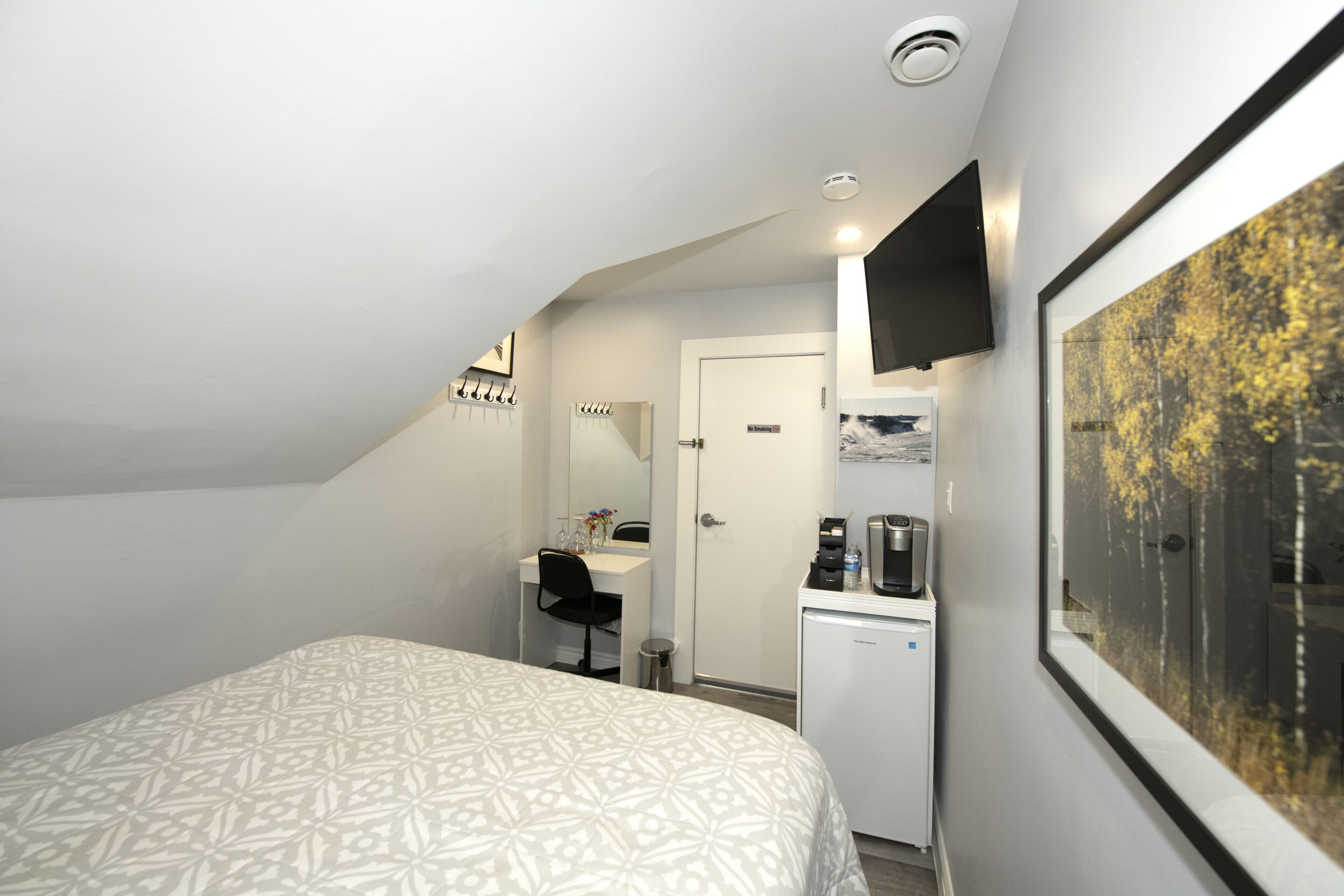 Quarto com cama, escrivaninha, espelho, máquina de café e quadro na parede.