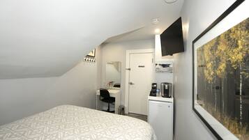 Quarto com cama, escrivaninha, espelho, máquina de café e quadro na parede.