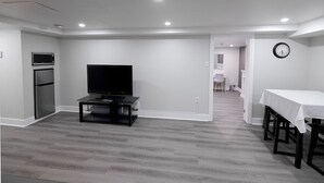 A modern living room with a flat-screen TV, a dining table, and a kitchen area with a microwave and refrigerator. - Serene Niagara Inn (Niagara Falls)