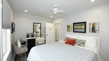 A hotel room with a large bed, a desk with a chair, a ceiling fan, and artwork on the walls.