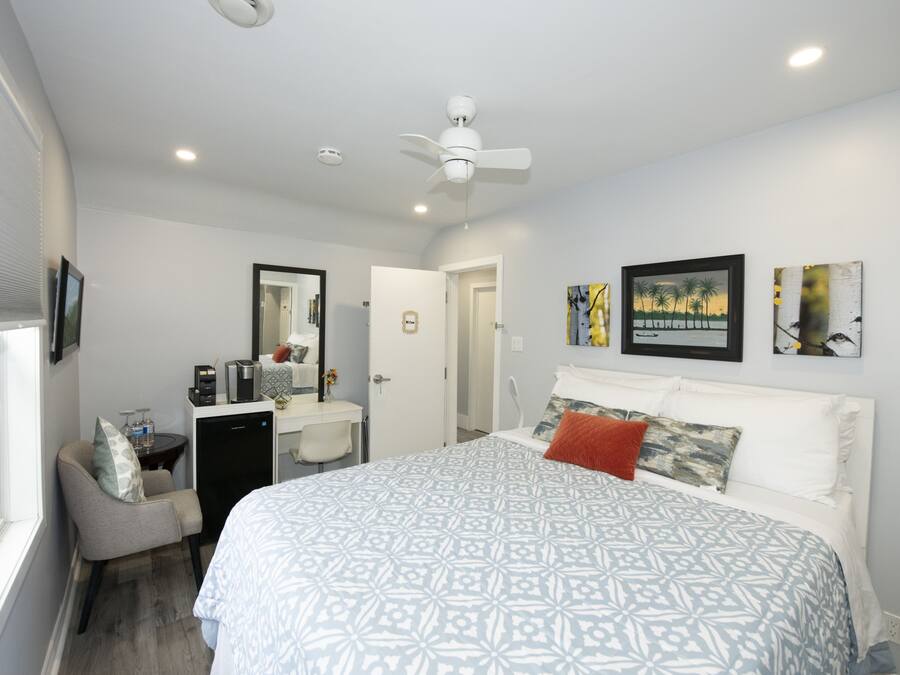 A hotel room with a large bed, a desk with a chair, a ceiling fan, and artwork on the walls.