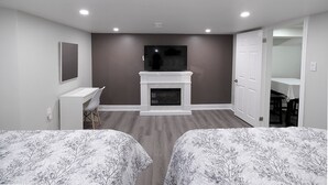 A bedroom with two beds, a desk, a fireplace, and a TV. - Serene Niagara Inn (Niagara Falls)