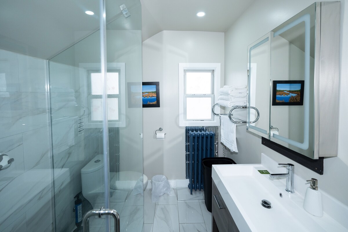 A modern bathroom with a glass shower enclosure, a white sink with a large mirror, and two framed pictures on the wall.
