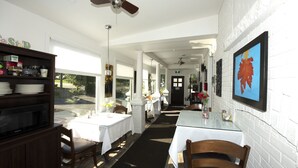 A restaurant with white brick walls, wooden furniture, and a ceiling fan. Tables are set with white tablecloths and chairs. - Serene Niagara Inn (Niagara Falls)