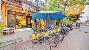 Entrada de un hotel con un letrero que dice "SON TRANG HOTEL", un paraguas azul y bicicletas con letreros de alquiler.
