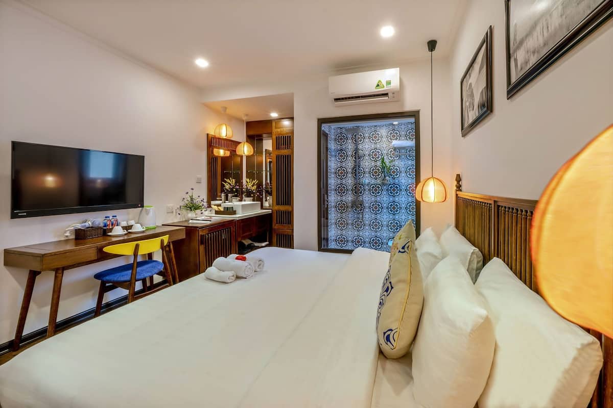 Hotellihuone, jossa on sänky, työpöytä tuolilla, televisio ja ilmastointilaite.