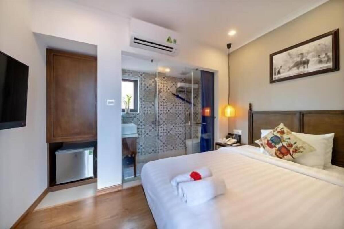 Hotelkamer met een bed, nachtkastje, wandtelevisie en zichtbare badkamer door een glazen deur.