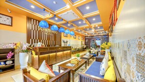 Un vestíbulo de hotel con muebles de madera, un mostrador de recepción y lámparas colgantes azules.