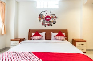 Una camera d'albergo con un letto, due comodini, una finestra e un elemento decorativo al muro.
