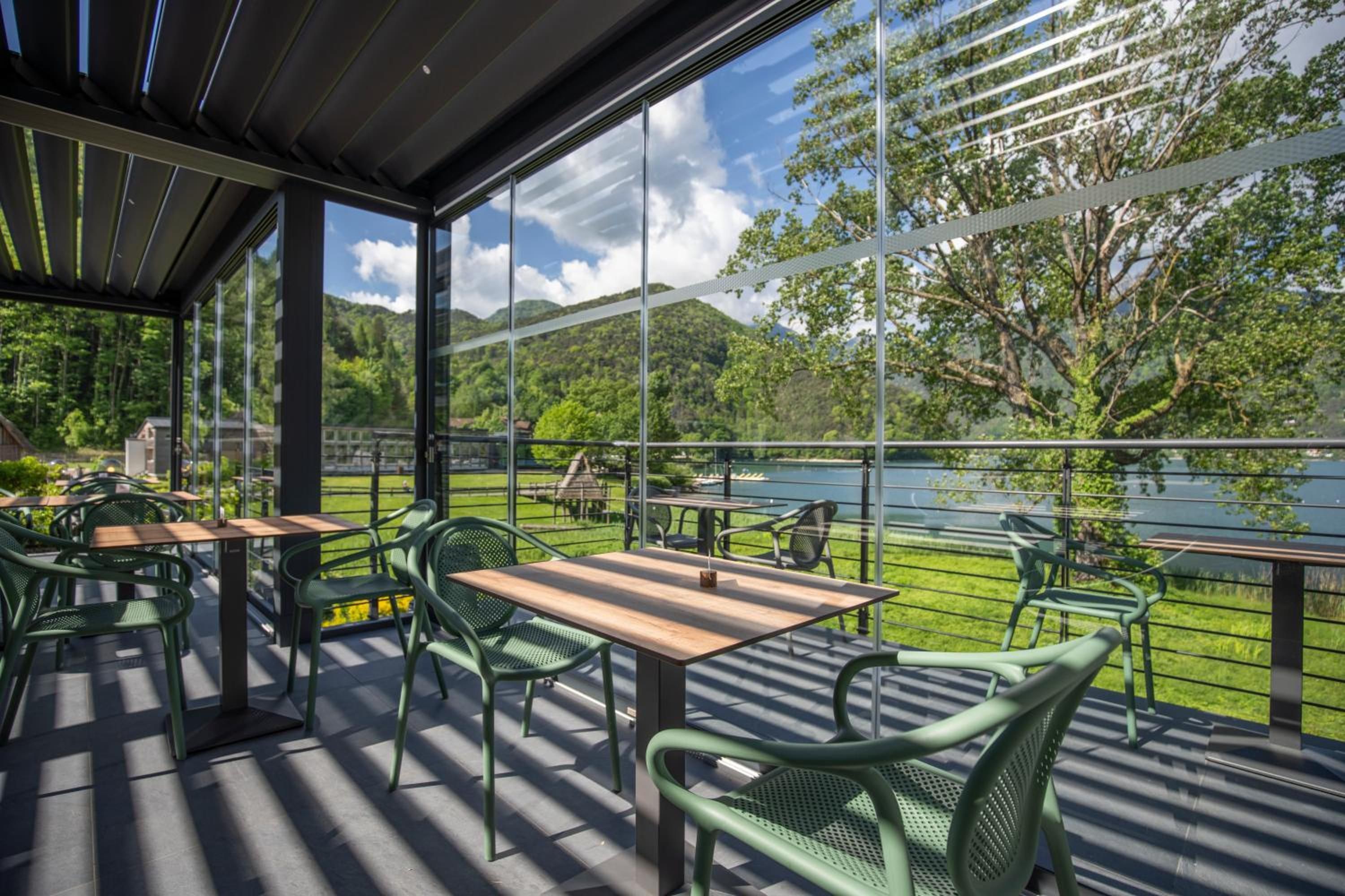 An outdoor seating area with tables and chairs, overlooking a lake and hills.
