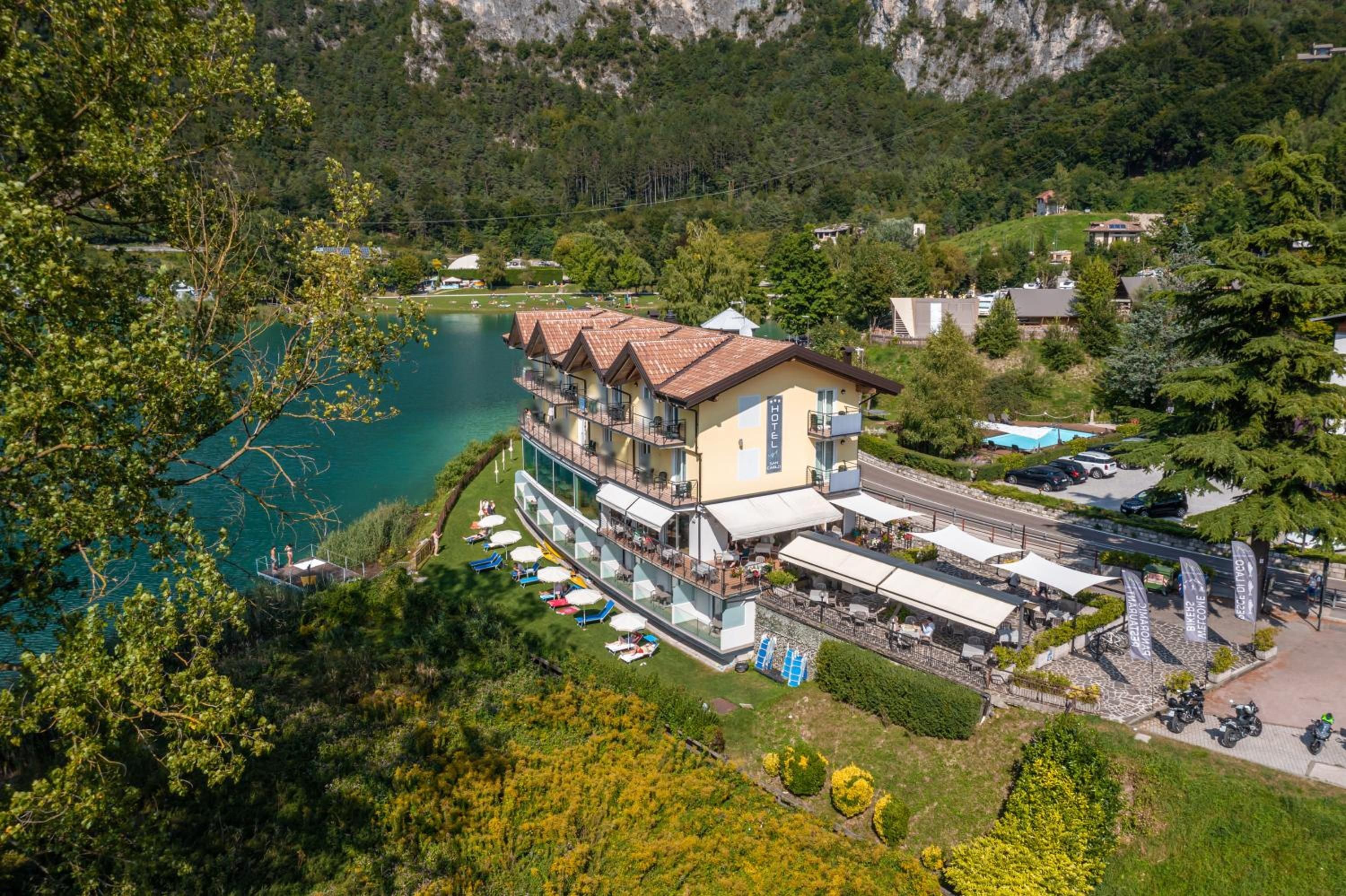 Un hotel con una terrazza che si affaccia su un lago, immerso nel verde e tra le colline.
