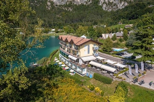 Un hotel con una terrazza che si affaccia su un lago, immerso nel verde e tra le colline.
