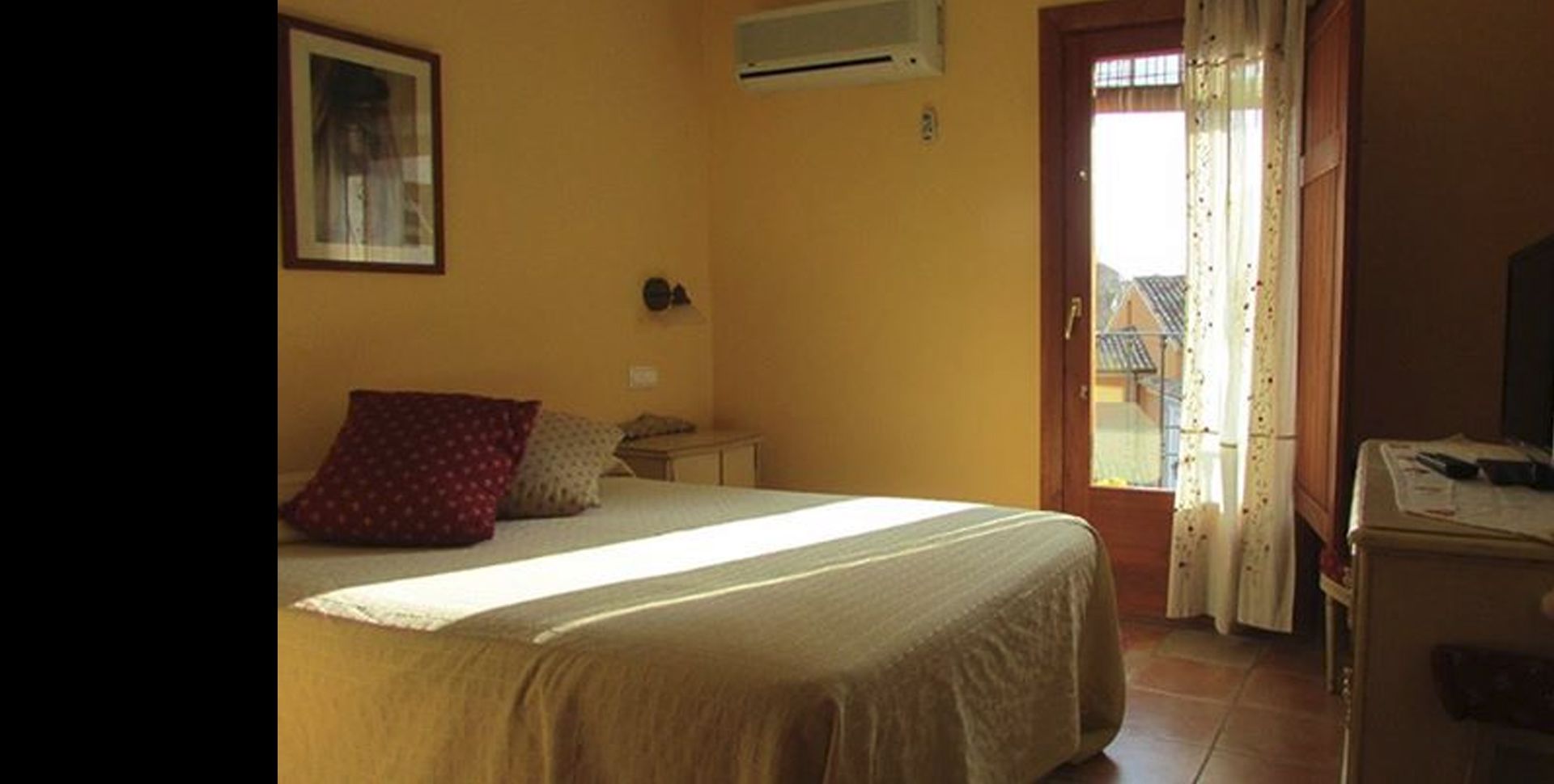 A bedroom with a bed, a nightstand, a desk, and a window with curtains.