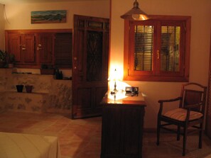 A cozy room with a wooden cabinet, a small table with a lamp, a chair, and a window with blinds. - Hostal de la Luz (Cuenca)