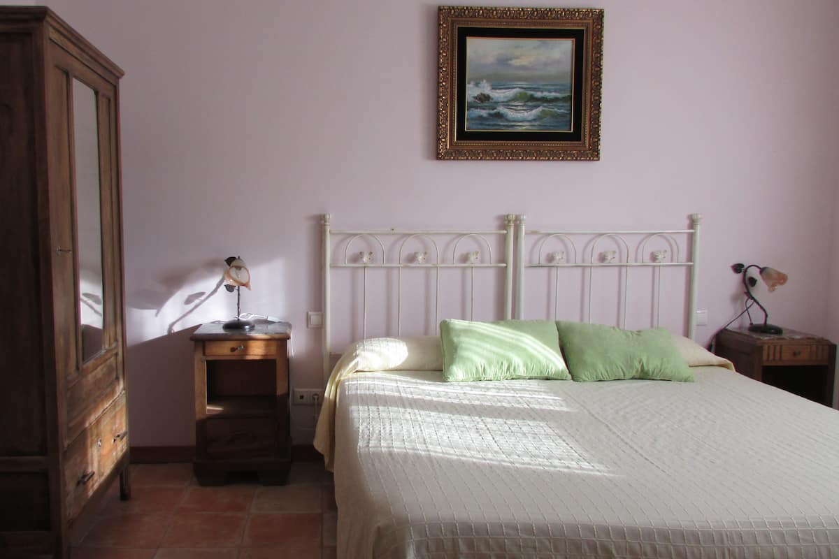 A bedroom with a bed, a nightstand, a dresser, a mirror, and a painting on the wall.