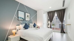 A modern bedroom with a bed, bedside tables, and a city view through large windows.