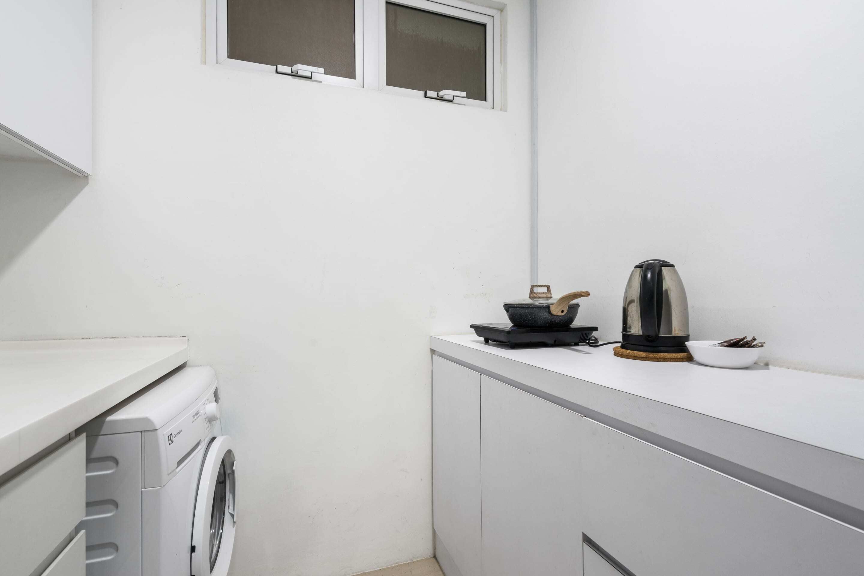 A compact kitchen with a washing machine, a kettle, and a small window.