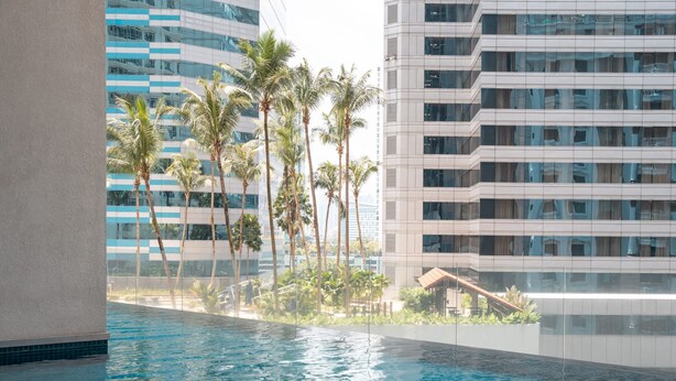 A modern building with a pool area, palm trees, and a view of other high-rise buildings.