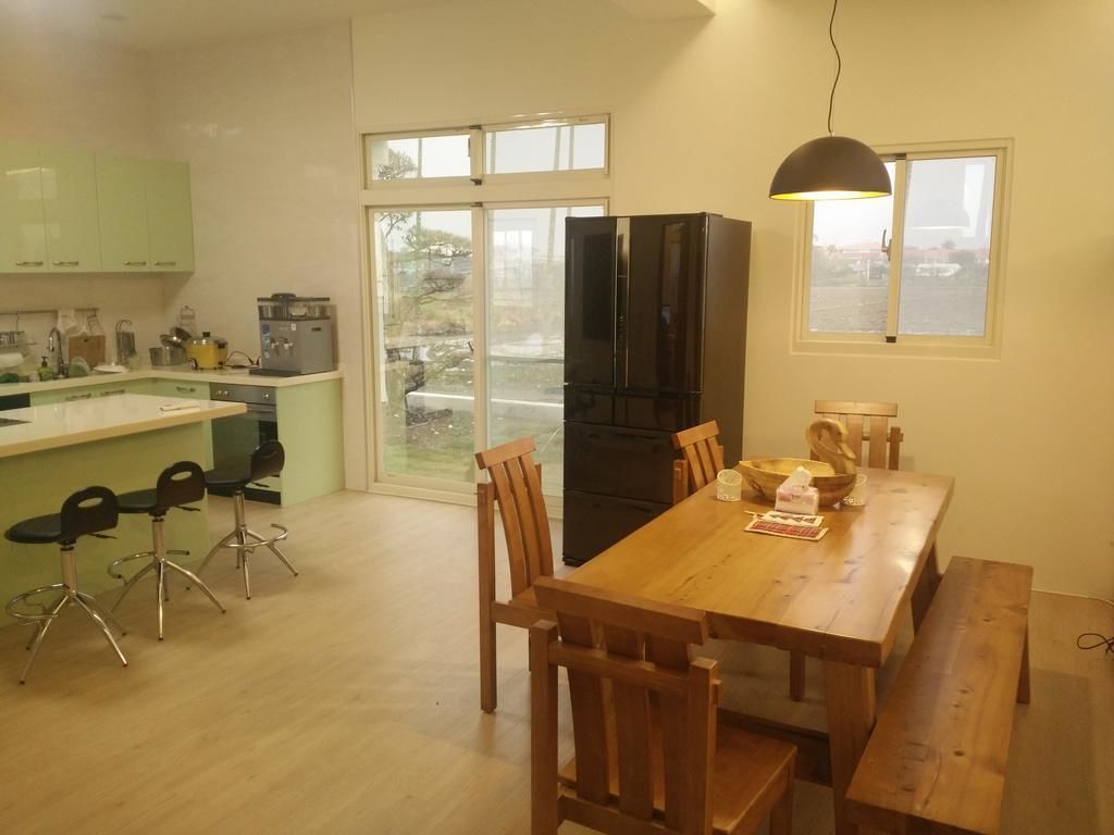 A modern kitchen with a dining area, wooden chairs, a black refrigerator, and a large window.