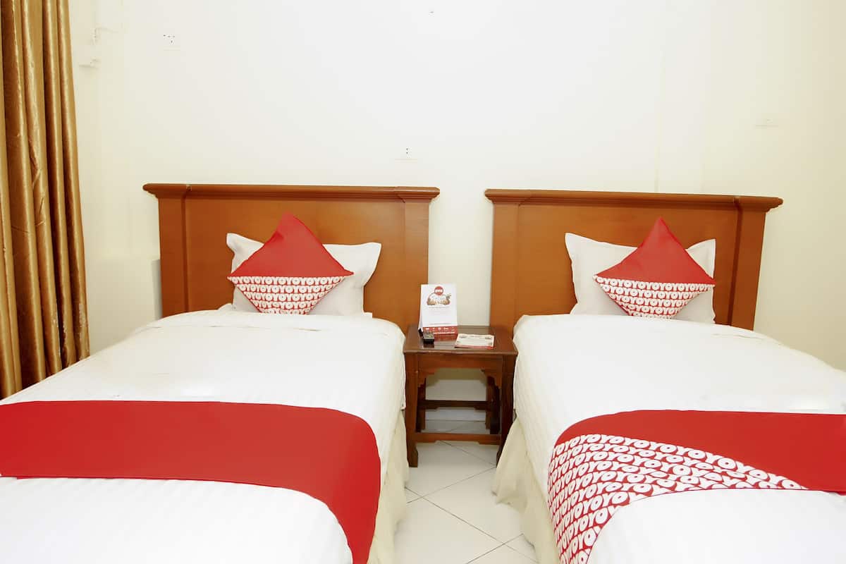 Ein Hotelzimmer mit zwei Betten, jeweils mit rot-weiß gestreifter Bettwäsche und passenden Kissen. Dazwischen befindet sich ein Nachttisch aus Holz mit Fernbedienung und Speisekartenständer.