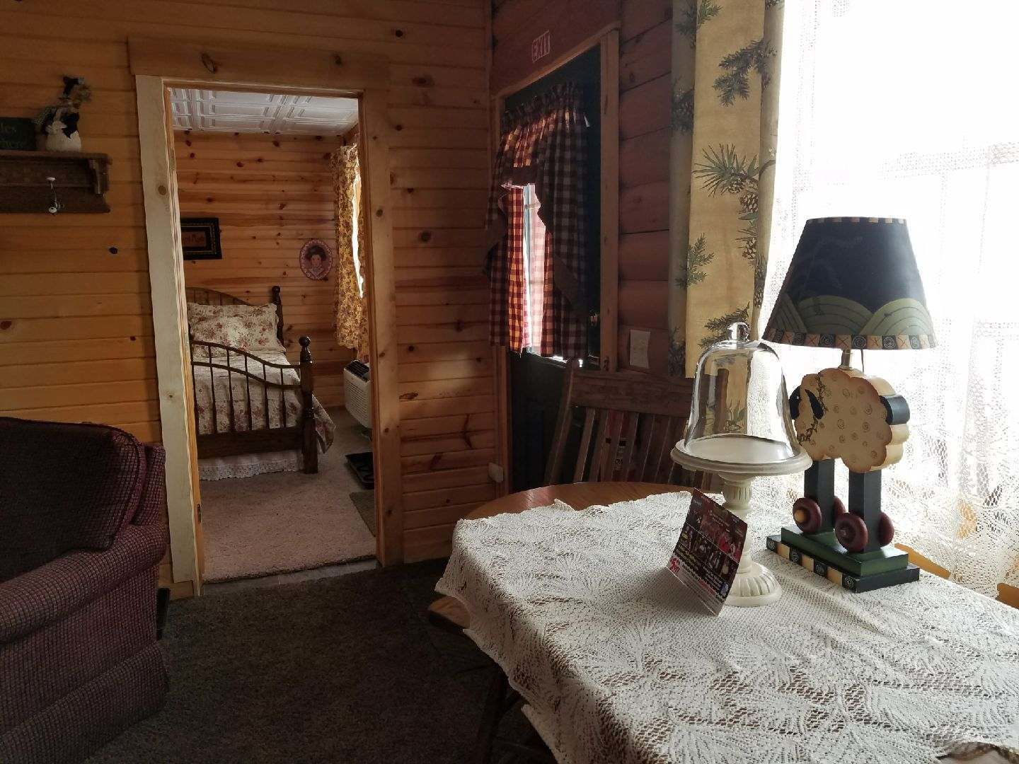 A cozy room with a wooden interior, a bed with a floral bedspread, a table with a lace tablecloth, and a lamp with a decorative shade.