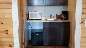 A compact kitchen with dark cabinets, a microwave, a coffee maker, and a small refrigerator. - Amish Blessings Cabins (Berlin)