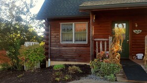 A wooden cabin with a green door, a window with a view, and a porch with plants. - Amish Blessings Cabins (Berlin)
