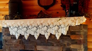 A stone fireplace with a lace mantel, a clock, and framed pictures on the wall above. - Amish Blessings Cabins (Berlin)