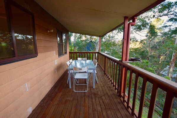 A wooden deck with a table and chairs, a railing, and a view of trees.