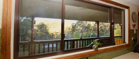 A kitchen with a large window, a wooden deck, and a green tiled backsplash.