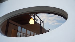 Une fenêtre circulaire avec un luminaire suspendu, une balustrade en bois et un aperçu de l’intérieur d’un bâtiment.