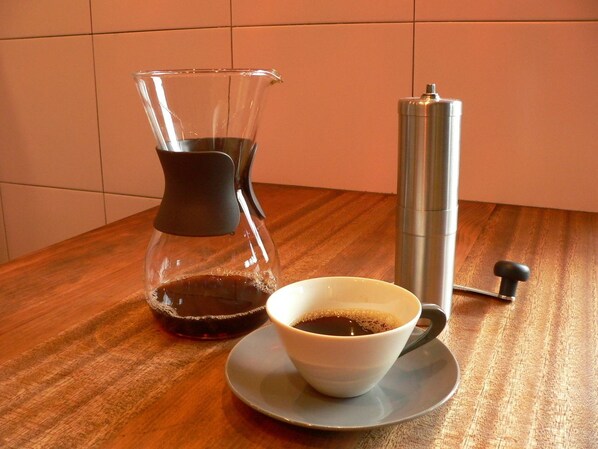 A coffee maker, a cup of coffee, and a thermos on a wooden table. - Moon's Cafe (Onomichi)