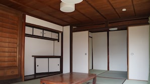 Une pièce de style japonais traditionnel, avec un sol recouvert de tatamis, une table en bois, des portes coulissantes et un ventilateur de plafond.