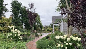 Um caminho no jardim leva a um edifício com fachada branca e varanda coberta.
