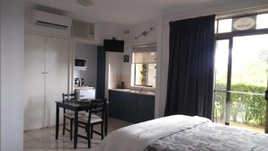 A hotel room with a bed, a desk, a kitchenette, and a balcony with curtains. - Banksia Park Estate (Newhaven)