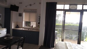A compact hotel room with a bed, a small kitchenette, a dining area, and a balcony with a view. - Banksia Park Estate (Newhaven)