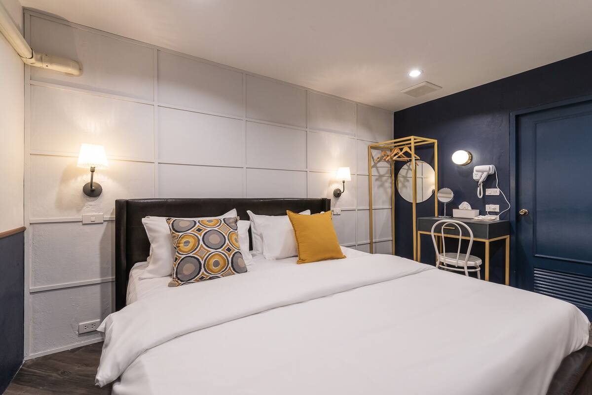 Una habitación de hotel ordenada con una cama grande, lámparas de noche, un escritorio con silla y un espejo.