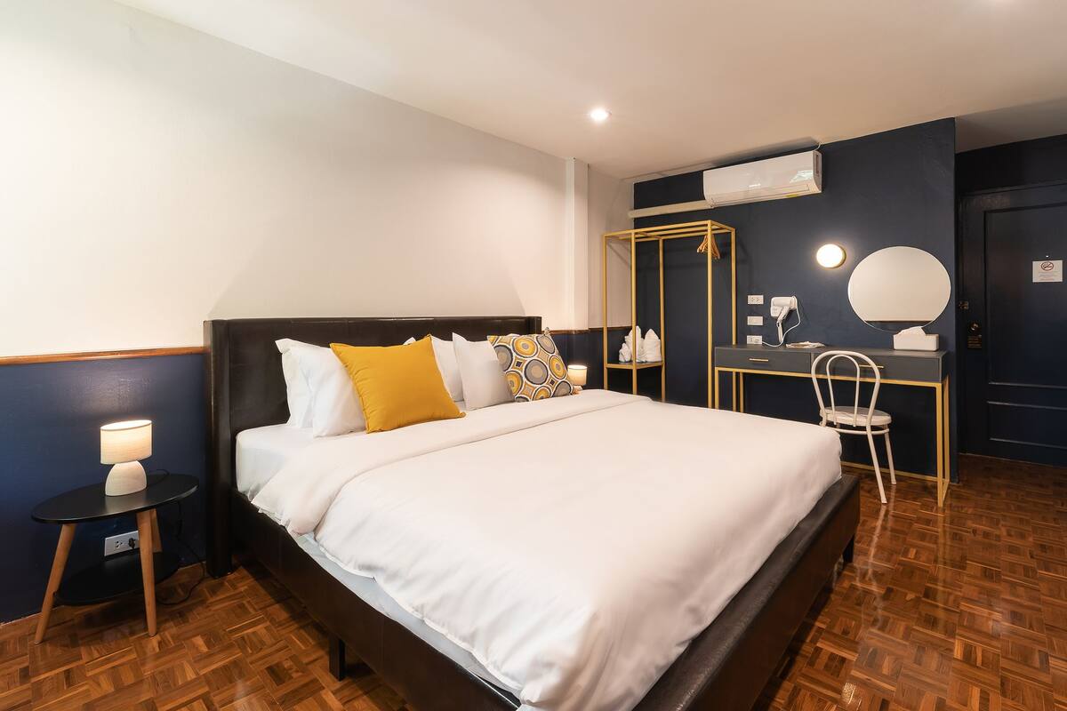 Habitación de hotel con una cama grande, un escritorio con silla, un espejo y un equipo de aire acondicionado.
