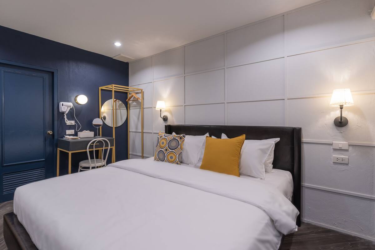 Habitación de hotel moderna con una cama grande, un escritorio con silla, un espejo y dos lámparas de pared.