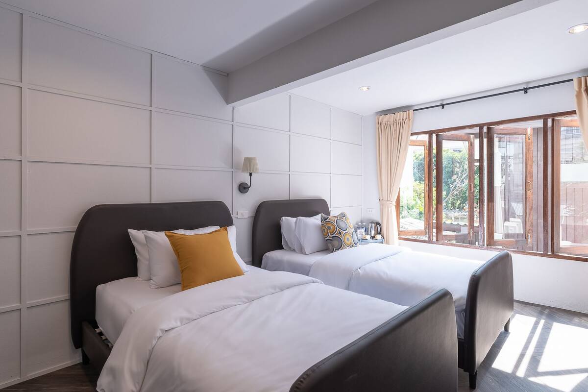 Una habitación de hotel con dos camas, un ventanal con cortinas y una lámpara en la pared.