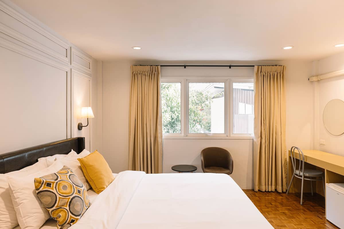 Habitación de hotel con cama, escritorio, silla y ventana con cortinas.